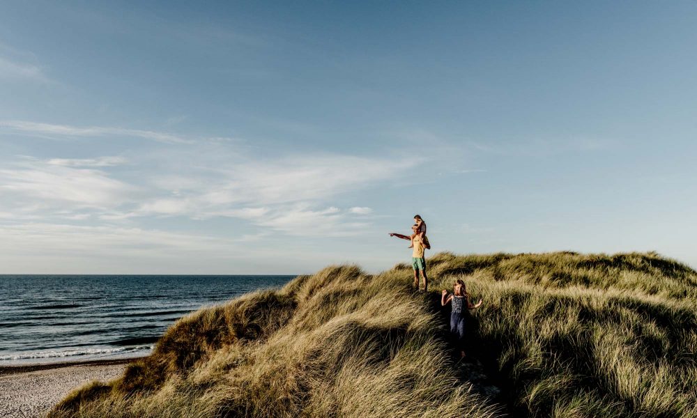 Far og to døtre i klitterne peger ud over havet