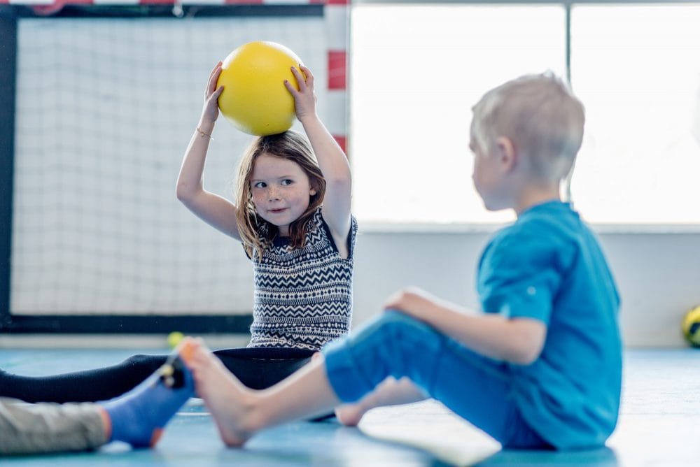 Dreng og pige sidder i gymnastiksal med bold