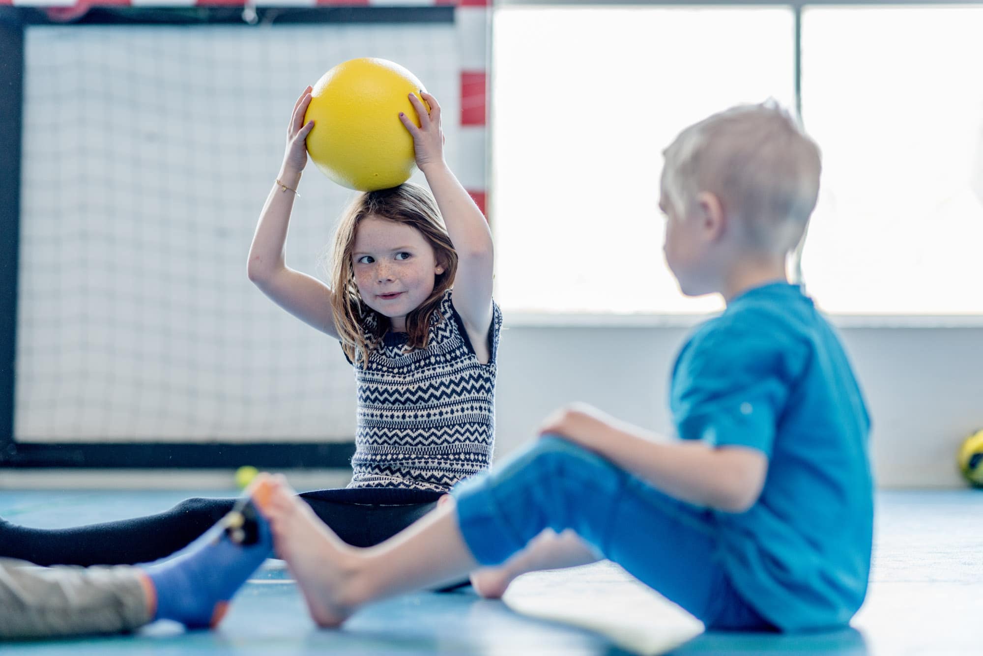 Dreng og pige sidder i gymnastiksal med bold