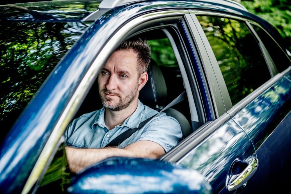 en mand kører i blå bil i en skov