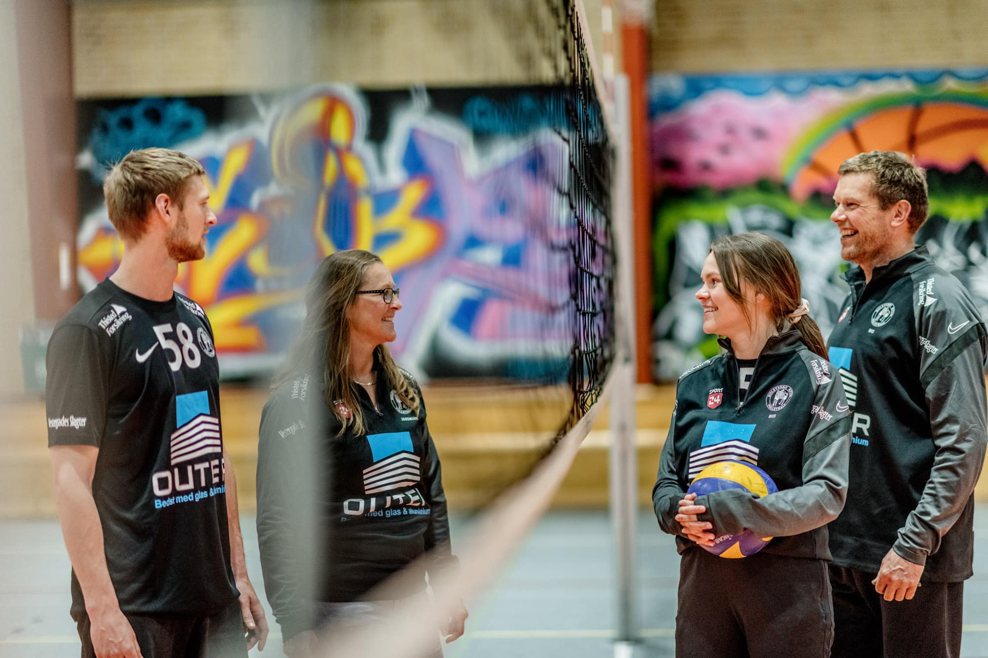 to mænd og to kvinder spiller volleyball i en hal