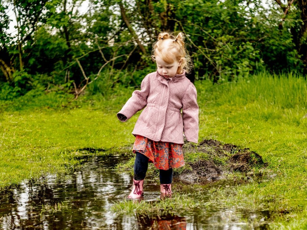 pige leger i vandpyt med lyserøde gummistøvler
