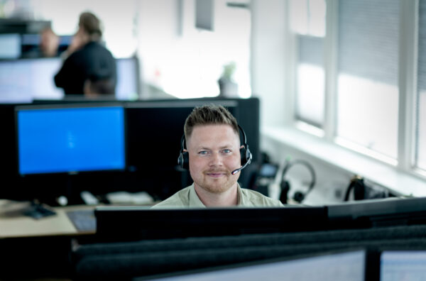 Mads er skademedarbejder hos Thisted Forsikring. Her sidder han ved sit skrivebord med headset på og smiler til kameraet.