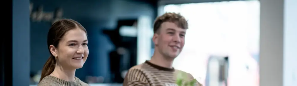 To finanselever, Line og Kristian, sidder i Thisted Forsikrings kantine og smiler.