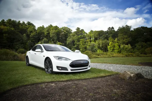 Tesla Model S holder på græsplæne med træer og himmel som baggrund.