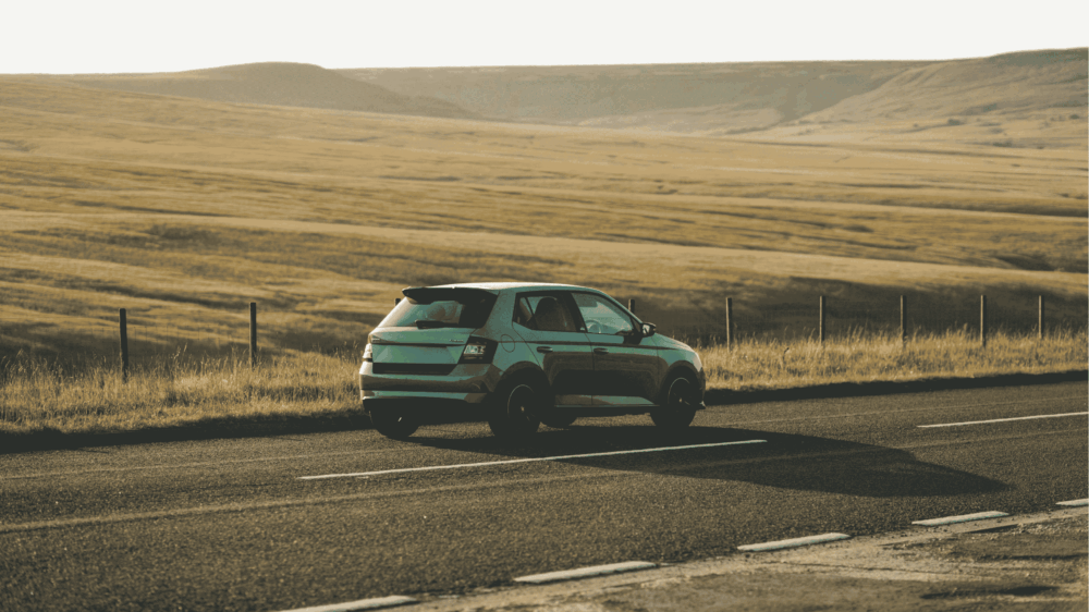 En Skoda kører på en landevej omgivet af marker.