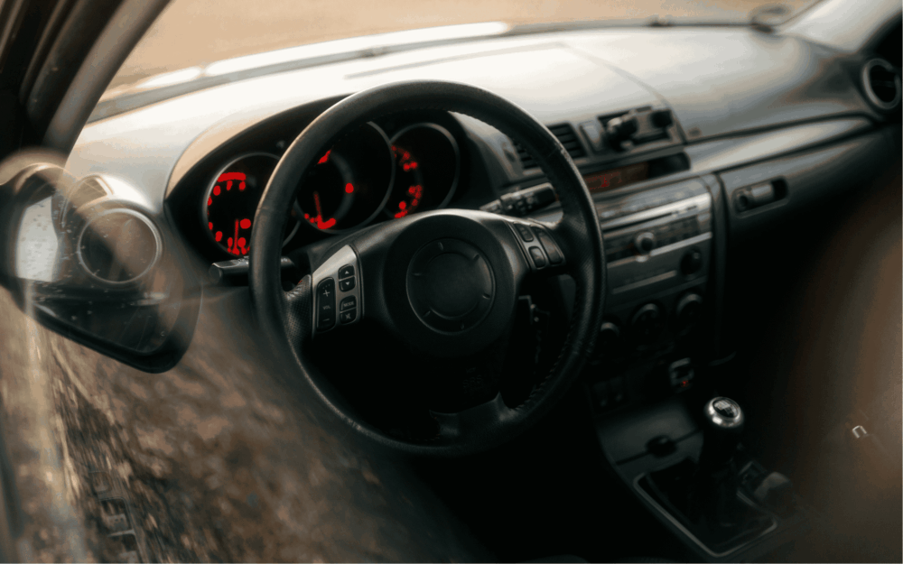 Indersiden af en Mazda. Rat og gearstang ses blandt andet.